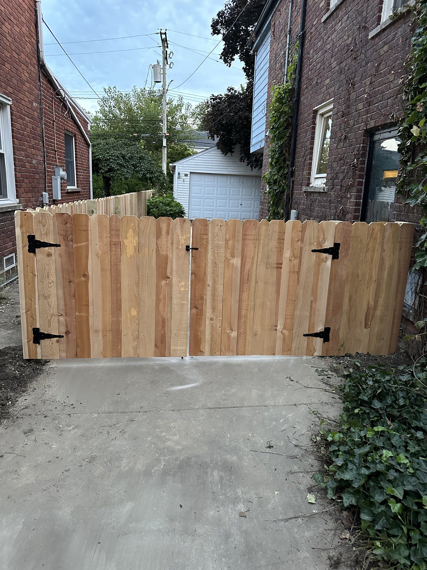 Wood double gate across a concrete driveway between two brick homes