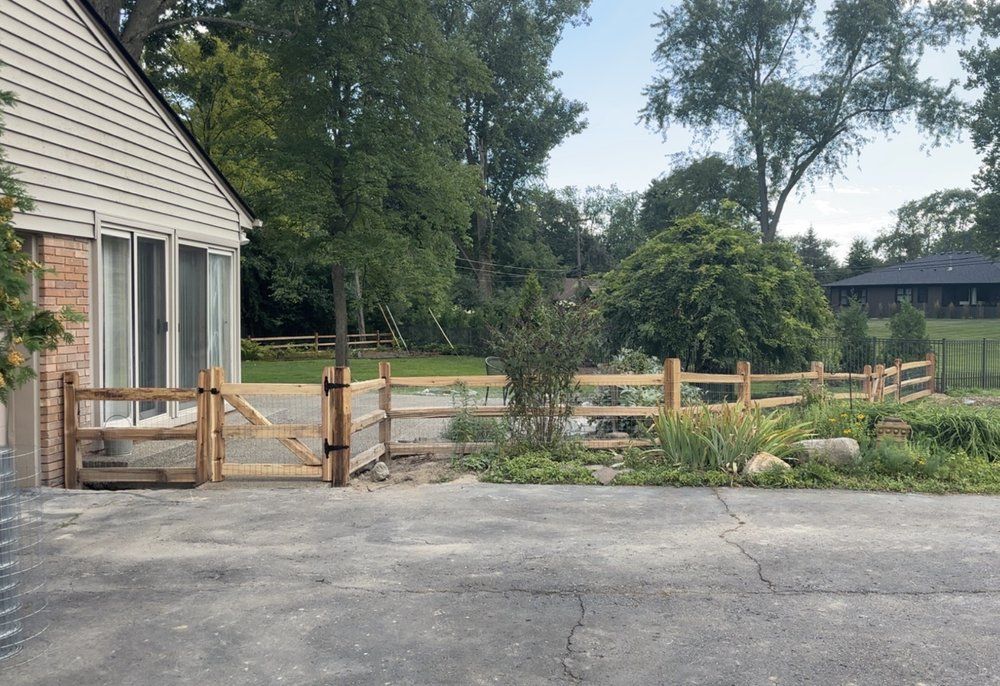 Wood split rail fence with a driveway gate in front of a ranch home